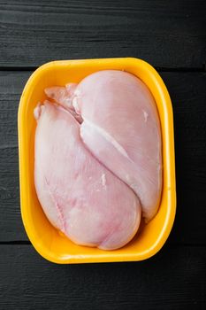 Fresh chicken breast meat in open tray, on black wooden table