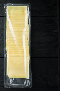 Slices of yellow cheese, sealed pack, on black wooden table with copy space for text