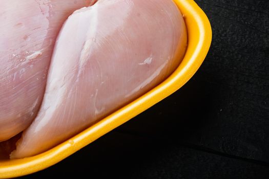 Fresh chicken breast meat in open tray, on black wooden table with copy space for text