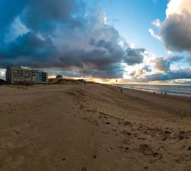 view on an empty beach of Sint-Idesbald in Koksijde at De Panne at sunset with a glowing cloudy sky with some people on it