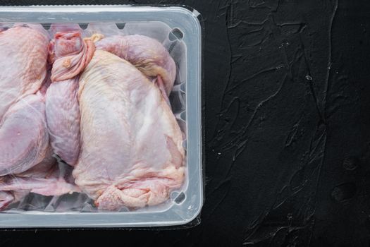 Raw chicken set in plastic vacuum tray, on black background, top view with copy space for text
