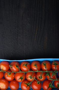 Red small cherry tomatoes, on black wooden table with copy space for text