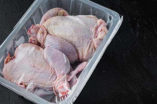 Raw chicken in plastic sealed plastic box, on black background with copy space for text