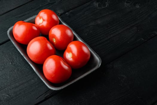Red tomatoes, on black wooden table with copy space for text