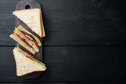 Sandwich with ham, cheese, tomatoe, lettuce, chicken meat and toasted bread, on black wooden table, top view with copy space for text