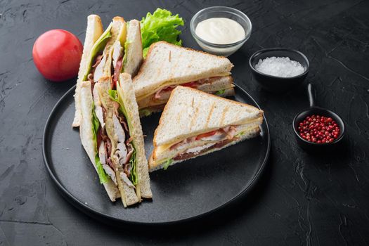 Homemade club sandwich made with turkey, bacon, ham, tomatoes, on black background