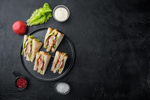 Homemade club sandwich made with turkey, bacon, ham, tomatoes, on black background, top view with copy space for text