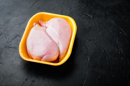 Raw chicken breast fillets in tray, on black background with copy space for text