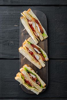 Homemade club sandwich made with turkey, bacon, ham, tomatoes, on black wooden table, top view