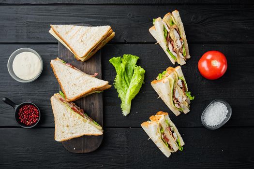 Homemade club sandwich made with turkey, bacon, ham, tomatoes, on black wooden background, top view