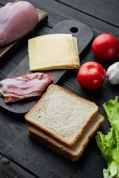 Ingredients for sandwich, bacon, cheese, tomato, chicken meat, lettuce, sauce, on black wooden table