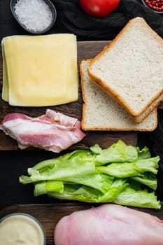 Ingredients for sandwich, bacon, cheese, tomato, chicken meat, lettuce, sauce, on black background, top view