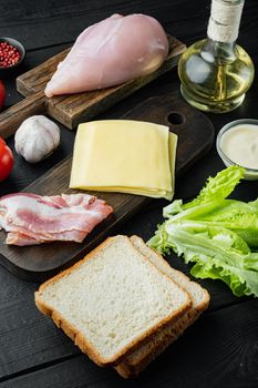 Ingredients for sandwich, bacon, cheese, tomato, chicken meat, lettuce, sauce, on black wooden background