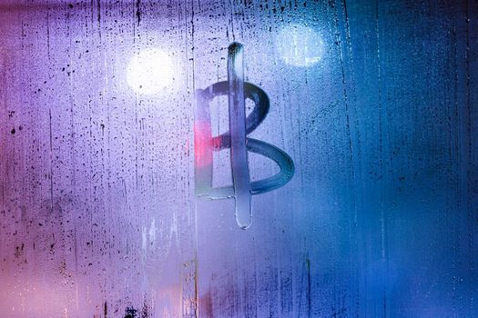 bitcoin symbol - handwritten on wet glass of night window, close-up with selective focus and background blur