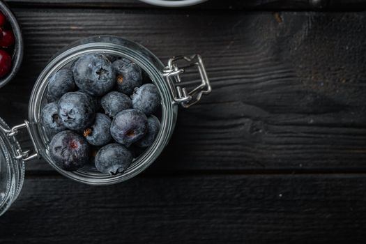 Ripe blueberry in glass jar, flat lay with space for text, on black wooden background.