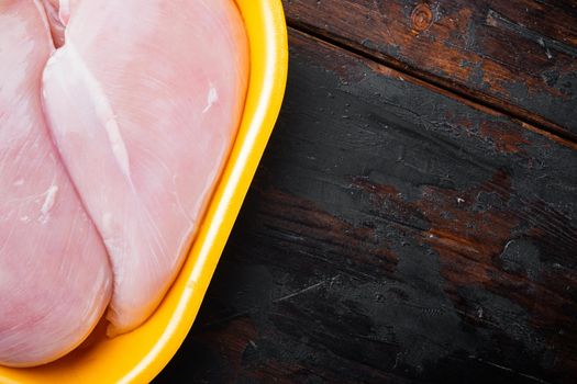 Fresh chicken breast meat in open tray, on dark wooden background with copy space for text