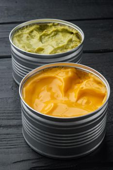 Canned cheese and guacamole sauce in can, on black wooden background