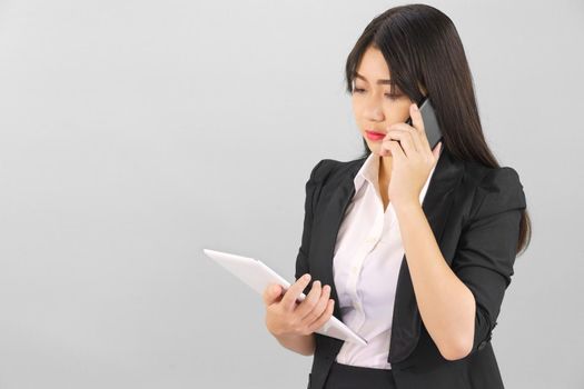 Young Asian women in suit standing using her digital tablet and phone against gray background