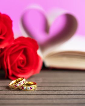 Pages of book curved into a heart shape with red rose and wedding ring . Love concept of heart shape from book pages