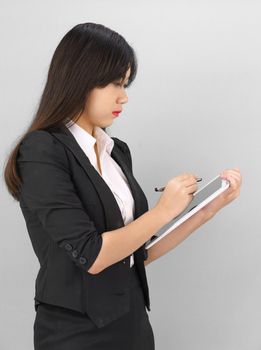 Young women in suit using her digital tablet standing against gray background