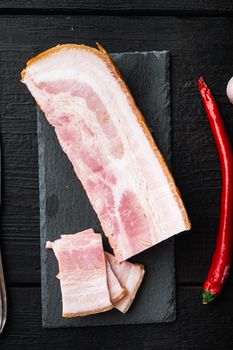 Smoked bacon, whole slab with herbs on black wooden table, top view.