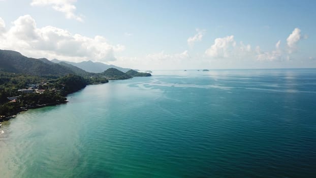 Clear water on the beach of green Chang Island. The turquoise color of the water reflects like a mirror the green hills of the island and the white clouds. Clean sand like in the Maldives. Thailand