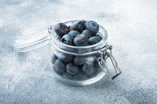 Ripe blueberry in glass jar, on textured background.