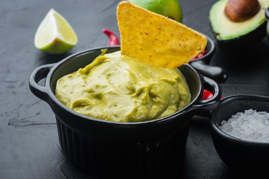 Creamy avocado dip with cilantro and lime in bowl, on black background