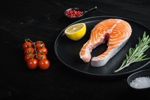 Raw trout steak with herbs, on black wooden surface.