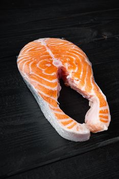 Salmon steak raw fish, on black wooden surface.