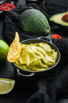 Avocado dip or guacamole in bowl, on black wooden background