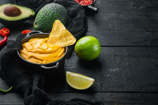 Bowl with cheese dip with nacho, on black wooden background with copy space for text