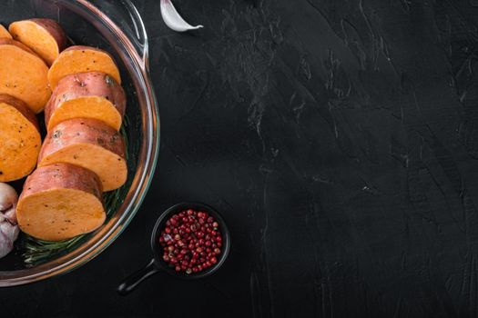 Cajun sweet potatoes for baking with herbs and spices on black background with copyspace.