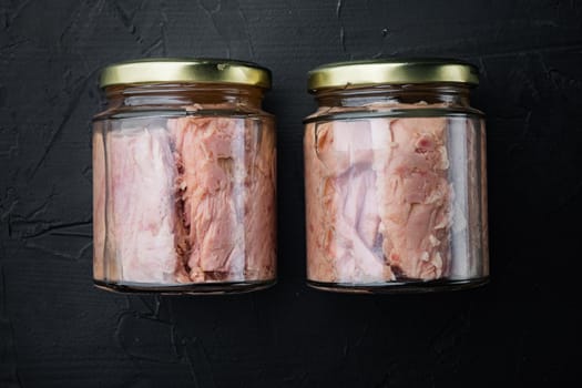 Tuna fillet meat in glass jar, on black background, flat lay