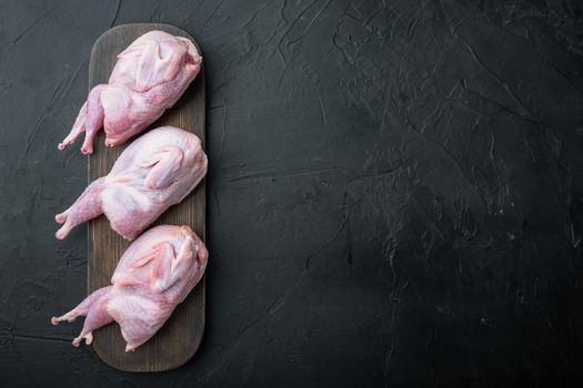 Raw uncooked quails set, top view, on black textured background with copy space