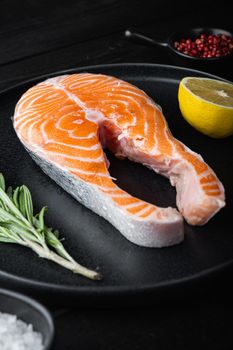 Fesh raw salmon fillet with herbs, on black wooden surface.