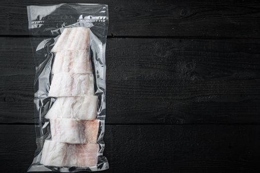 Raw haddock fish skinless plastic vacuum packaged, on black wooden background, top view with copy space for text