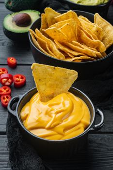 Nachos corn tortilla chip with cheese dip sauce, on black wooden background