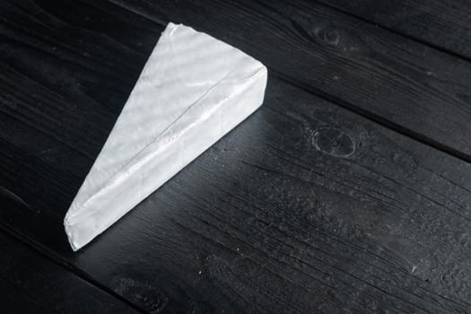 Piece of the brie cheese set, on black wooden background with copy space for text