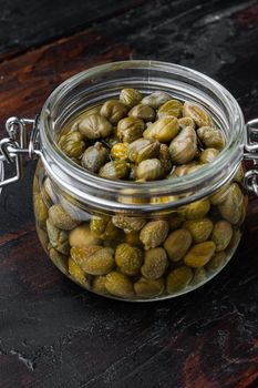 Baby capers in marinate glass jar, on dark wooden background