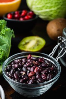Red beans in bowl with healthy food on dark wooden background.