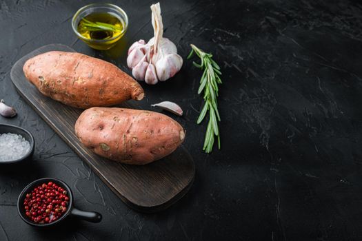Raw whole sweet potatoe with herbs and spices on black background with copyspace.