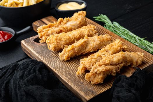 Crispy chicken tenders cuts on black wooden background.
