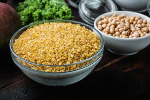 Bulgur grain in bowl on dark wooden background.