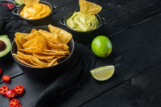 Triangular yellow corn tortilla chip with sauces, on black wooden background with copy space for text