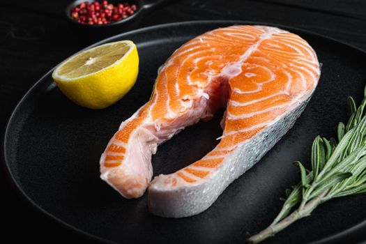 Slice of red fish salmon with herbs, on black wooden surface.