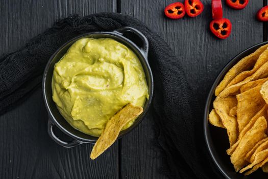 Nachos corn tortilla chip with avocado dip or guacamole in bowl, on black wooden background, top view or flat lay