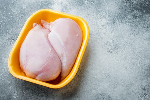 Fresh chicken breast meat in open tray, on gray background with copy space for text