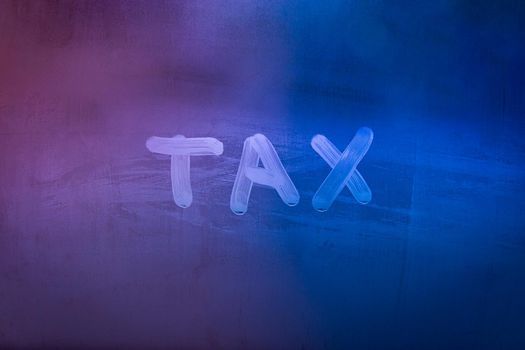 word tax hadwritten on night wet window glass surface with blue and purple colors in blurry background