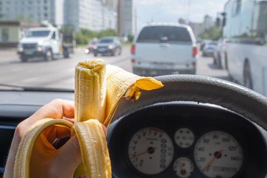 Food, banana in the hand of a driver driving a car that is driving on a city street among city traffic